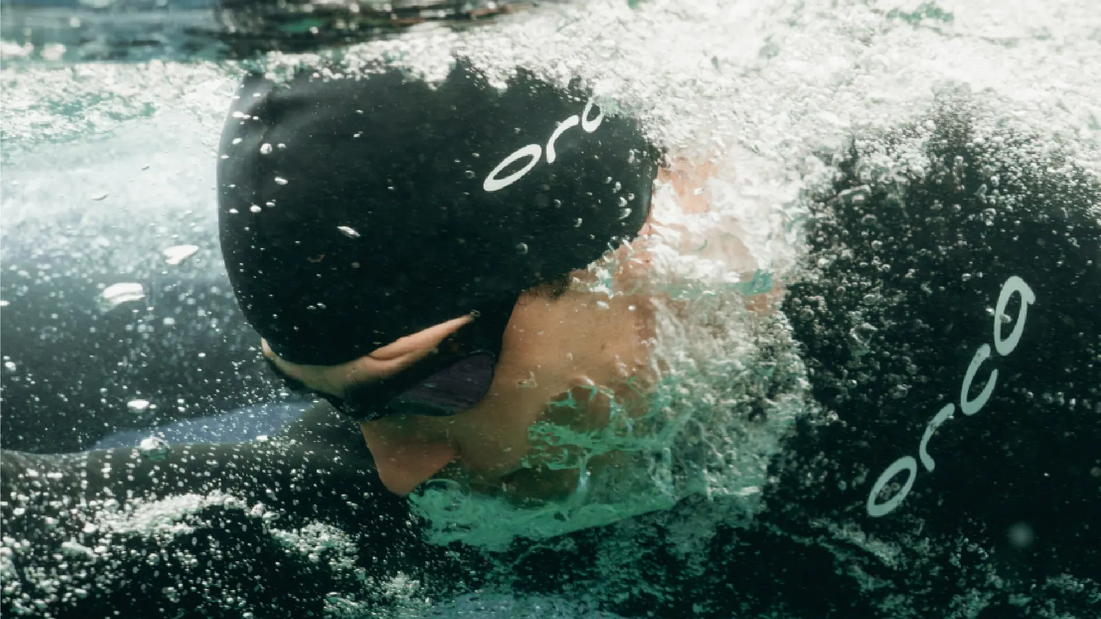 Schwimmer unter Wasser mit Orca-Badekappe und Neoprenanzug